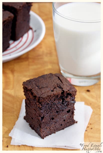 A chocolate banana brownie on baking paper beside a glass of milk